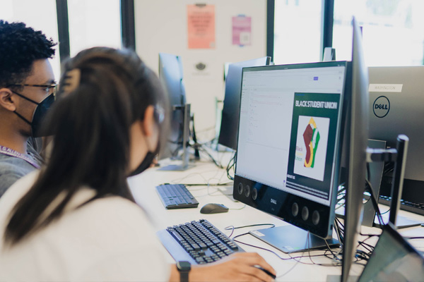 Diversity & Access photo featuring students sitting at a desk with compute screens